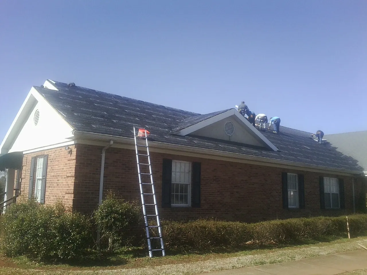 Crew tearing shingles off a brick ranch roof with a ladder set — Metal Roof Repair work by our crew in Coupeville