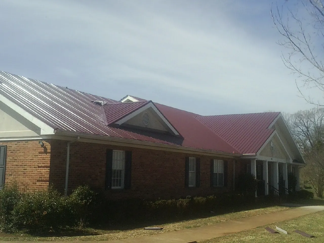 Red metal roof with gabled entries on a long brick building, from a Hail Damage Roof Repair job in Coupeville