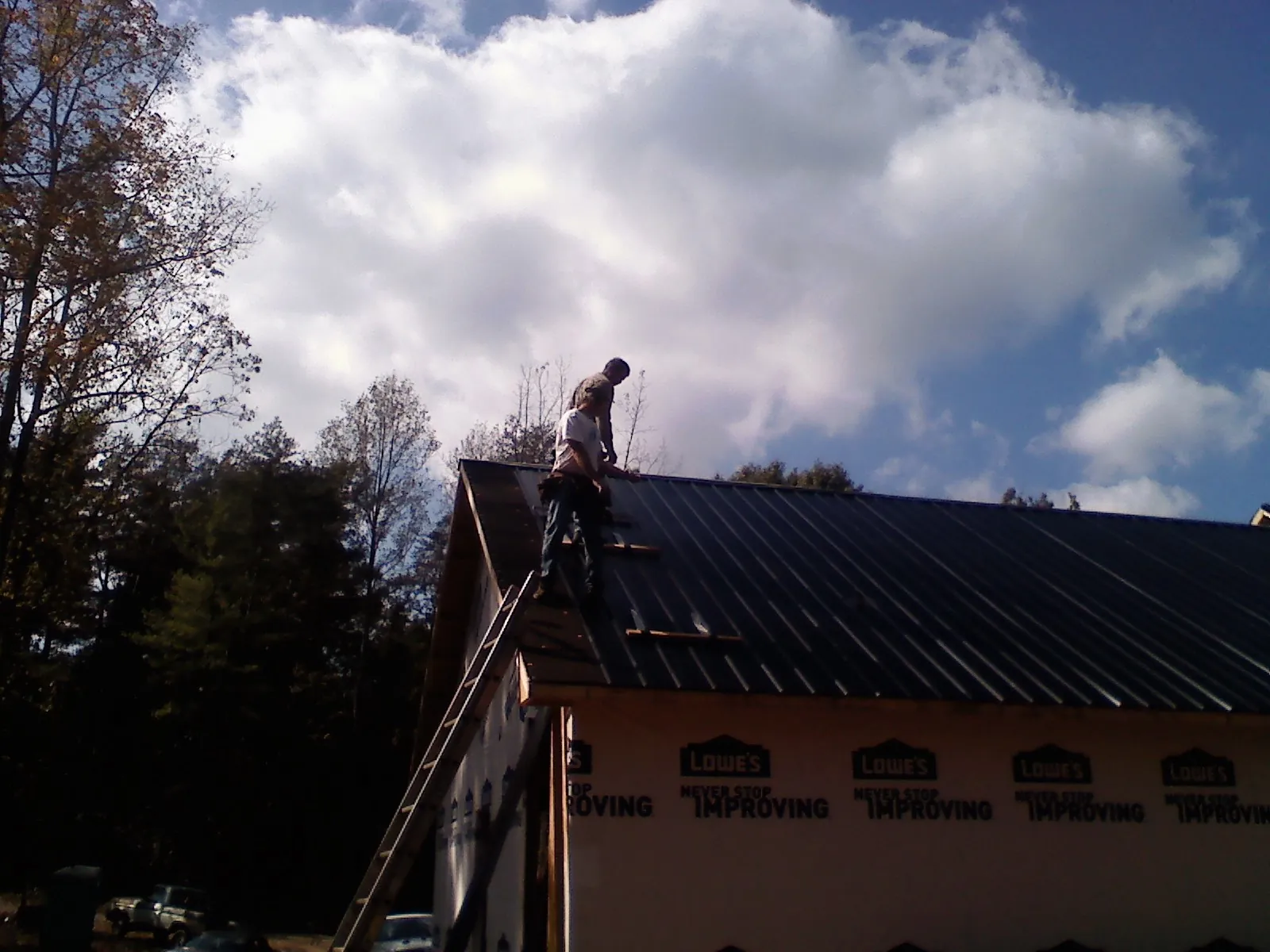 Roofer fastening dark metal panels high against a cloudy sky, from a Roof Inspection job in Coupeville