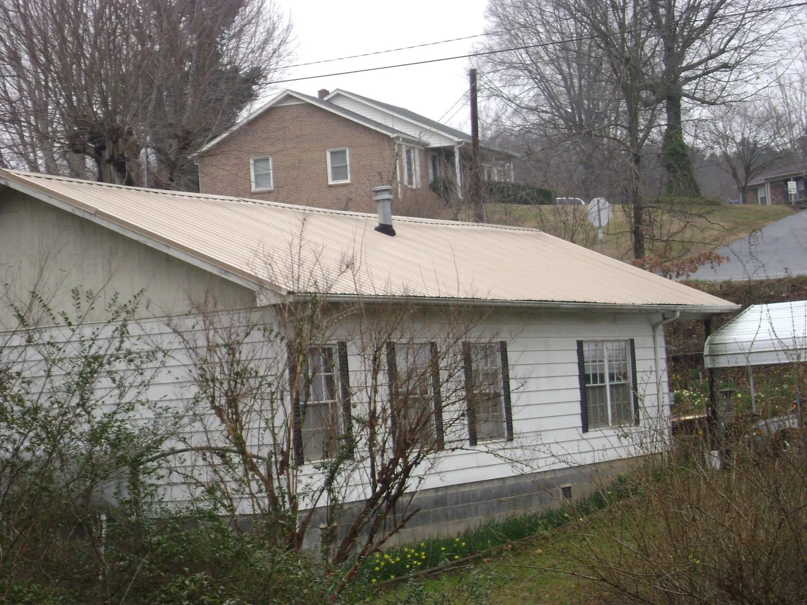 Tan metal roof on a white sided house set into a hillside — Commercial Roofing by Roofing Brothers in Coupeville